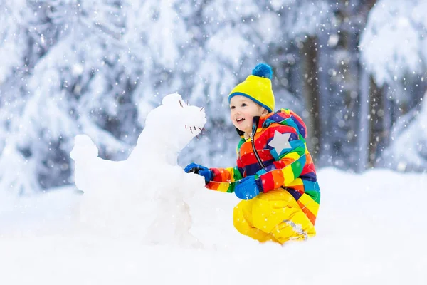 在雪冬公园里做雪人的孩子 孩子们在雪地里玩耍 小男孩在五颜六色的夹克和帽子大厦雪恐龙在冬天庭院在雪以后 冷冬日的户外娱乐 — 图库照片