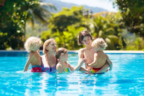 Family in swimming pool. Kids swim in outdoor infinity pool of tropical resort during summer vacation. Parents and children in water. Summer fun. Mother, teenager, toddler and baby learning to swim.