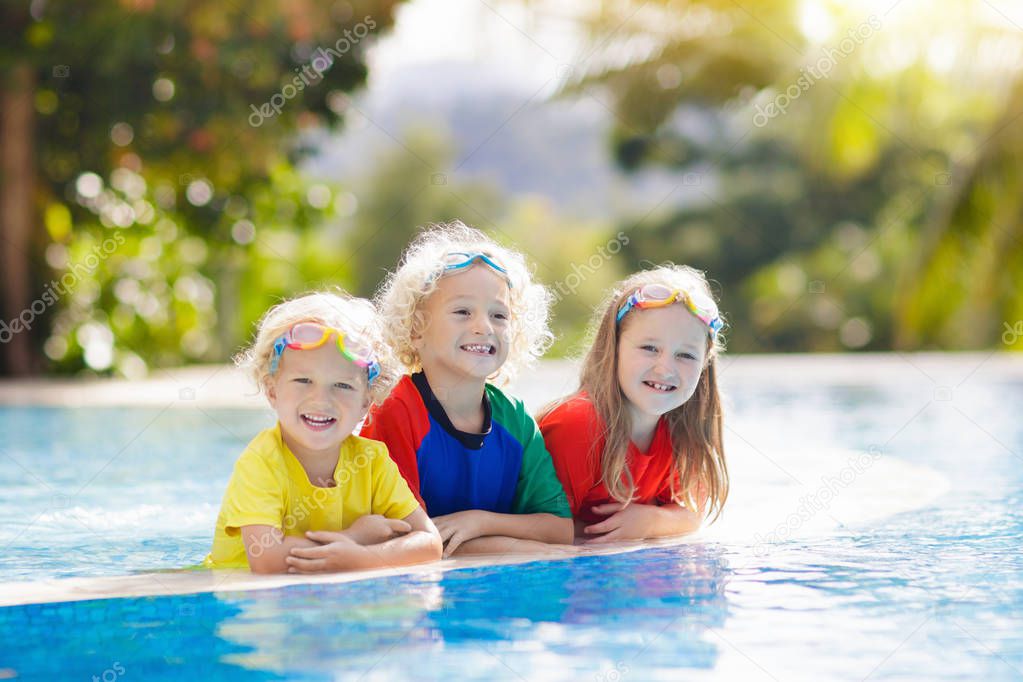 Kids play in swimming pool. Children learn to swim in outdoor pool of tropical resort during family summer vacation. Water and splash fun for young kid on holiday. Sun protection for child and baby.