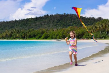Tropikal plaj renkli uçurtma ile çalışan çocuk. Çocuk uçan gökkuşağı uçurtma. Oyuncak uçak ile deniz kıyısında oynayan küçük bir kız. Egzotik ada aile yaz tatili. Su ve kum eğlenceli çocuklar için. 