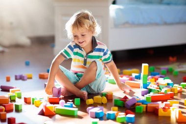 Çocuk renkli oyuncak bloklarıyla oynuyor. Çocuklar oynar. Küçük çocuk güneşli beyaz yatak odasındaki karanlık zeminde oyuncaklardan kule inşa ediyor. Bebek ve bebek için eğitici bir oyun. Çocuklar oyuncak ev yapar.