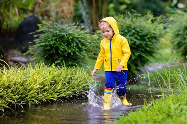 孩子们在秋天公园的雨中玩耍 孩子们在泥泞的水坑里跳跃 穿着雨靴和黄色夹克的小男孩在外面大雨倾盆 儿童防水鞋和外套 — 图库照片