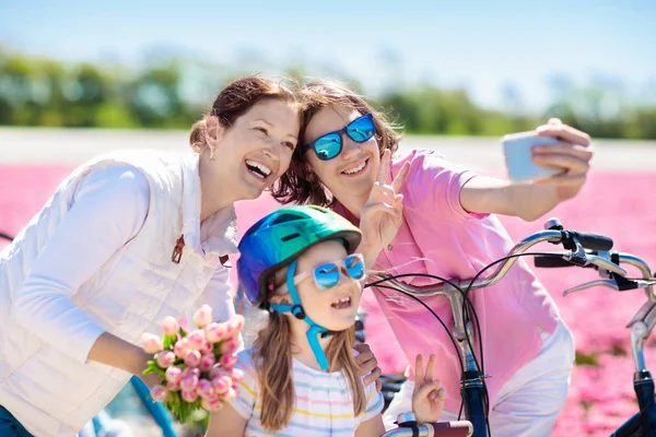 荷兰家庭骑自行车在郁金香花卉领域在荷兰 在荷兰盛开的郁金香上 母亲和孩子们带着手机摄像头在自行车上自拍照片 父母和孩子骑自行车 — 图库照片