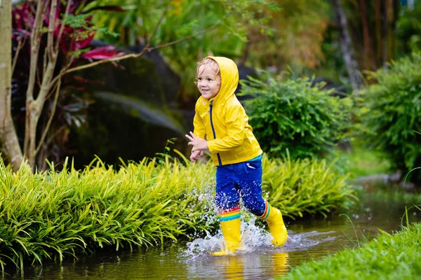 孩子们在秋天公园的雨中玩耍 孩子们在泥泞的水坑里跳跃 穿着雨靴和黄色夹克的小男孩在外面大雨倾盆 儿童防水鞋和外套 — 图库照片