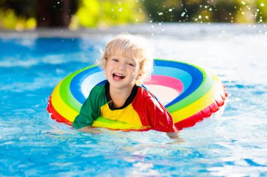 Yüzme havuzunda yüzen bir çocuk. Çocuklar yüzer. Genç çocuklar için renkli gökkuşağı yüzüyor. Küçük çocuk yaz tatilinde tropik tatil köyünde eğleniyor. Plaj ve su oyuncakları. Güneş koruması.