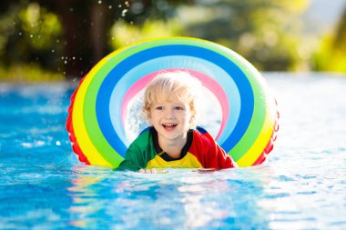 Yüzme havuzunda yüzen bir çocuk. Çocuklar yüzer. Genç çocuklar için renkli gökkuşağı yüzüyor. Küçük çocuk yaz tatilinde tropik tatil köyünde eğleniyor. Plaj ve su oyuncakları. Güneş koruması.