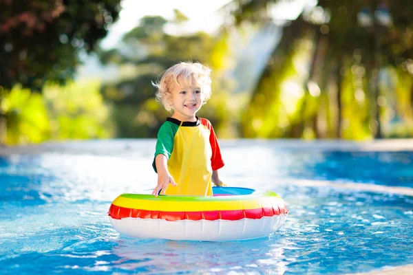 子供のプールおもちゃのリングに浮かんでいます 子供たちは泳ぐ 子供のためのカラフルな虹のフロート トロピカルリゾートで家族の夏休みを楽しんでいる小さな男の子 ビーチや水のおもちゃ 太陽の保護 — ストック写真