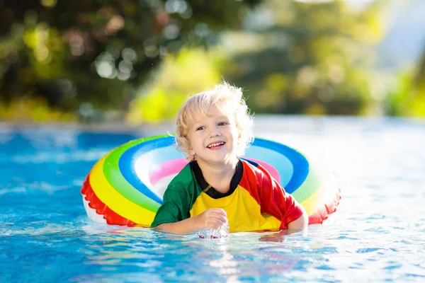 子供のプールおもちゃのリングに浮かんでいます 子供たちは泳ぐ 子供のためのカラフルな虹のフロート トロピカルリゾートで家族の夏休みを楽しんでいる小さな男の子 ビーチや水のおもちゃ 太陽の保護 — ストック写真