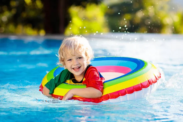 在游泳池里的孩子漂浮在玩具环上 孩子们游泳 五彩缤纷的彩虹飘浮在小孩身上 小男孩在热带度假胜地的家庭暑假玩得很开心 海滩和水玩具 — 图库照片