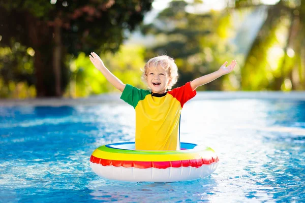 在游泳池里的孩子漂浮在玩具环上 孩子们游泳 五彩缤纷的彩虹飘浮在小孩身上 小男孩在热带度假胜地的家庭暑假玩得很开心 海滩和水玩具 — 图库照片