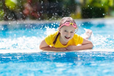 Çocuk havuzda oynuyor. Çocuklarla yaz tatili. Tropik bir adada egzotik tatilde suya atlayan küçük bir kız. Çocuklar yüzer. Anaokulu öncesi için aktif açık hava sporu.