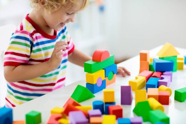 Renkli oyuncak blokları ile oynayan çocuk. Küçük çocuk blok oyuncaklar kulesi inşa. Eğitim ve yaratıcı oyuncaklar ve oyunlar genç çocuklar için. Bebek gökkuşağı tuğla ile beyaz yatak odasında. Oyuncak üzerinde odaklanmak.