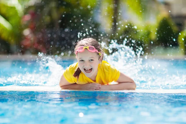 Çocuk havuzda oynuyor. Çocuklarla yaz tatili. Tropik bir adada egzotik tatilde suya atlayan küçük bir kız. Çocuklar yüzer. Anaokulu öncesi için aktif açık hava sporu.
