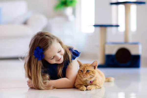 孩子在家里和猫玩耍 孩子和宠物 小女孩喂着可爱的姜黄猫 爱抚它 客厅里的猫 树和刮胡刀 孩子们玩和喂猫 家养动物 — 图库照片