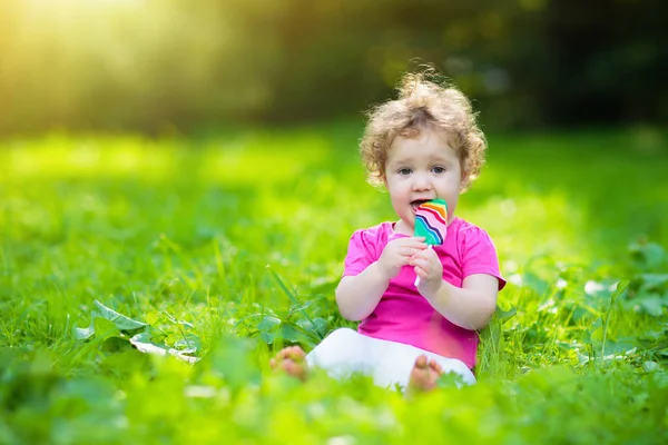 在阳光明媚的公园里吃冰淇淋糖果的女婴 带棒棒糖的孩子 孩子们在夏天在户外玩耍 幼儿与甜食 孩子们吃糖果 不健康的糖治疗的孩子 — 图库照片