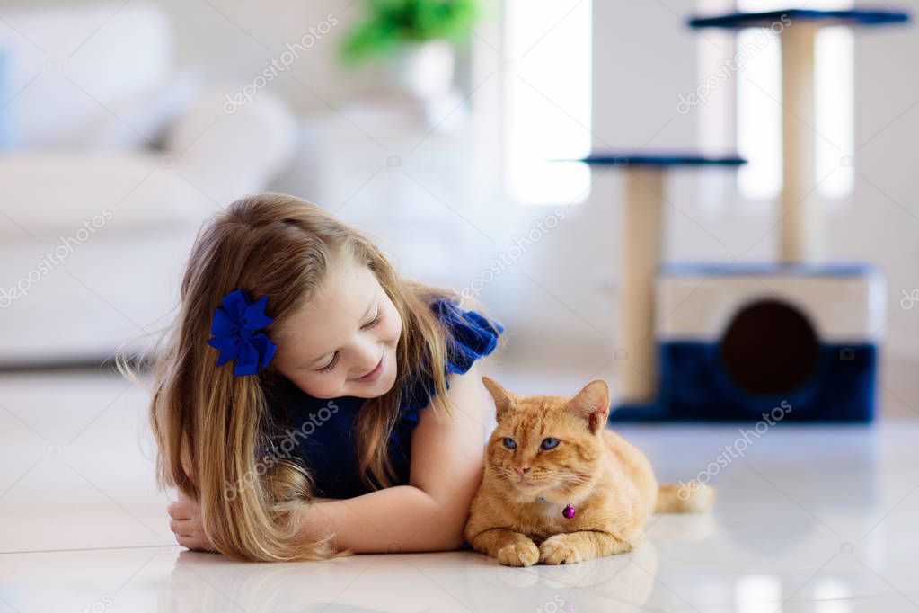 Child playing with cat at home. Kids and pets. Little girl feeding and petting cute ginger color cat. Cats tree and scratcher in living room interior. Children play and feed kitten. Home animals.
