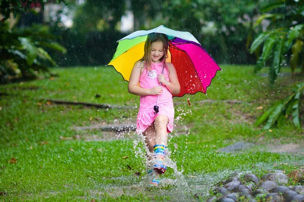 Kind mit Regenschirm spielt im Sommerregen. — Stockfoto