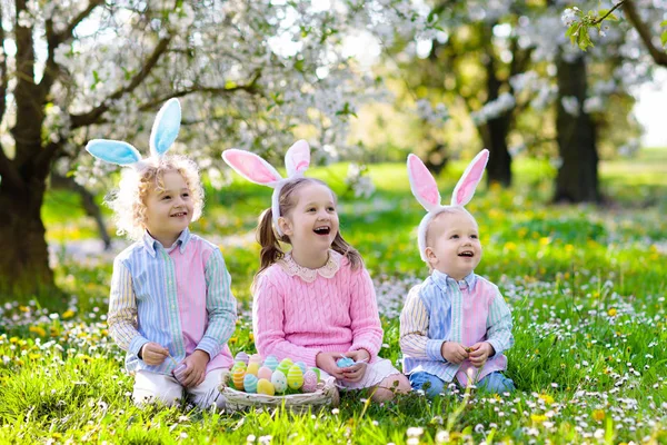 Eieren zoeken met Pasen. Kinderen met bunny oren en mand. — Stockfoto