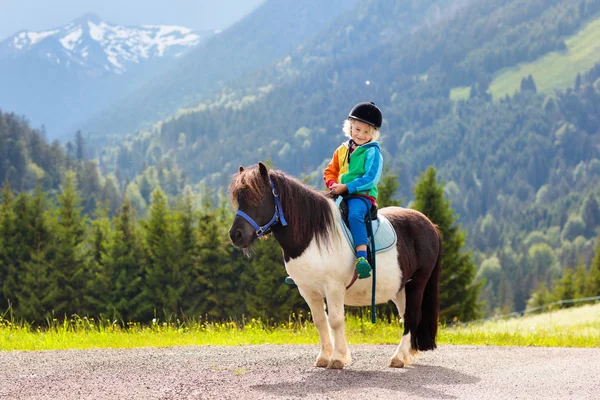 Miúdos a montar pónei. Criança a cavalo nas montanhas dos Alpes — Fotografia de Stock