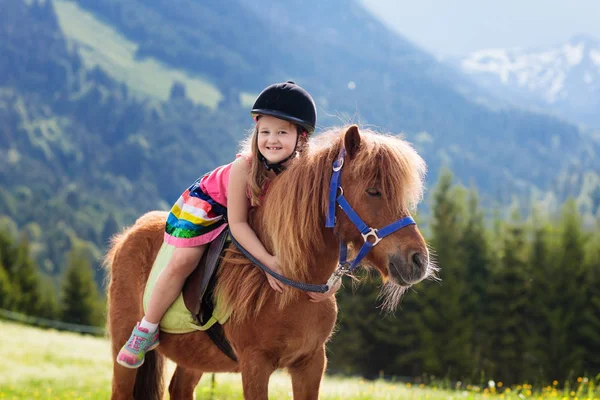 Niños montando pony. Niño a caballo en los Alpes montañas —  Fotos de Stock