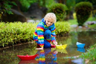 Su birikintisinde kağıt tekneli çocuk. Yağmurla çocuklar.