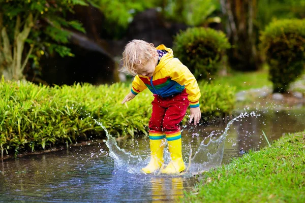 水たまりで遊ぶ子供。子供たちは秋の雨の中でジャンプ — ストック写真