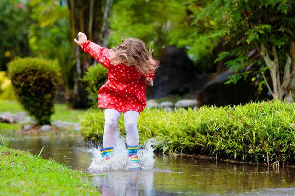 Niño jugando en el charco. Los niños saltan bajo la lluvia de otoño — Foto de Stock