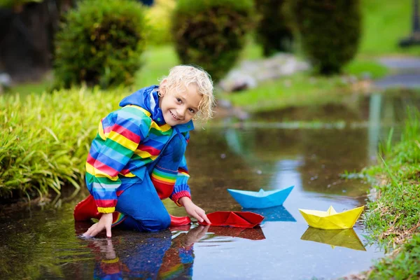 Dziecko z papierową łodzią w kałuży. Dzieci przez deszcz. — Zdjęcie stockowe