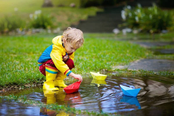 Niño con barco de papel en charco. Niños por la lluvia . —  Fotos de Stock