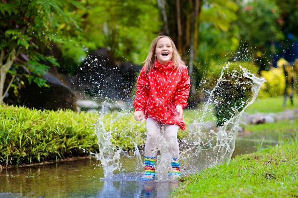 水たまりで遊ぶ子供。子供たちは秋の雨の中でジャンプ — ストック写真