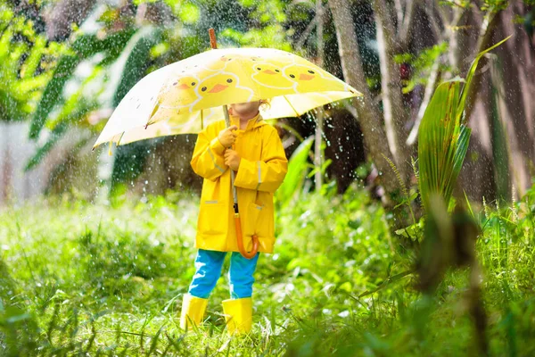 Bambino che gioca sotto la pioggia. Ragazzo con ombrello . — Foto Stock