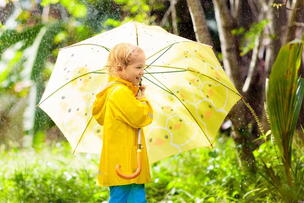 Bambino che gioca sotto la pioggia. Ragazzo con ombrello . — Foto Stock