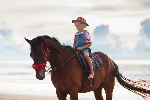 Enfants chevauchant à cheval sur la plage. Les enfants montent à cheval . — Photo