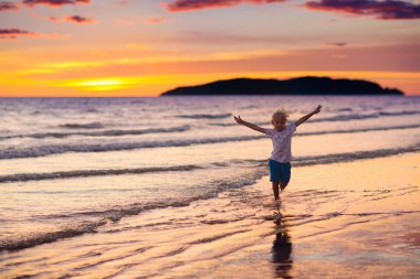 Okyanus plaj üzerinde oynayan çocuk. Gün batımı denizde evlat.