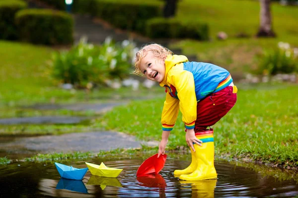 Niño con barco de papel en charco. Niños por la lluvia . — Foto de Stock