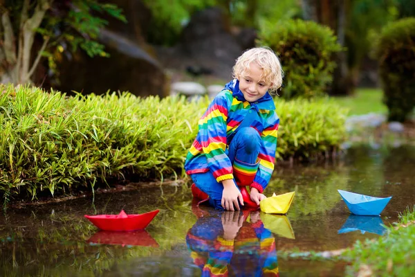 Bambino con barca di carta in pozzanghera. Bambini dalla pioggia . — Foto Stock