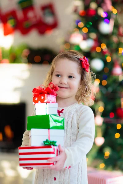 Kleines Mädchen öffnet Weihnachtsgeschenke am Kamin — Stockfoto