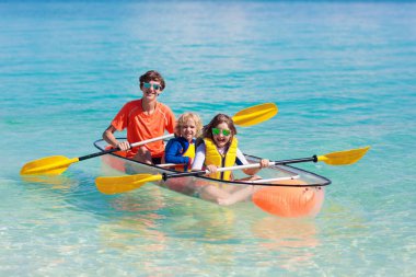 Çocuklar okyanusta kayak yapıyor. Tropikal denizde kanodaki çocuklar. Genç bir çocukla aktif tatil. Ebeveynler, küçük bir oğlan ve güzel bir sahilde kanodaki bir kız. Çocukla birlikte tatil aktivitesi. Aile suyu eğlencesi.