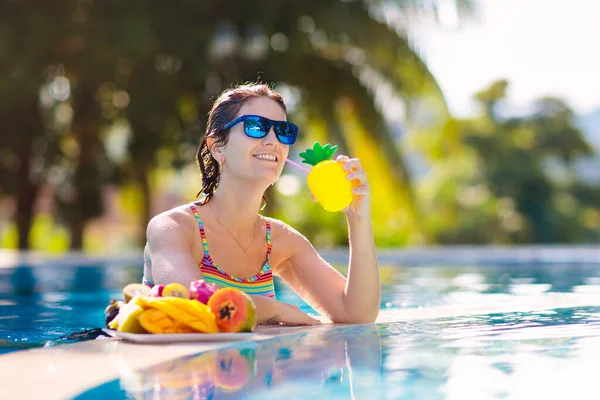 Tropical fruit plate at swimming pool. Young woman eating mango, pineapple, orange and drinking fresh juice on summer vacation at exotic island. Healthy nutrition. Beach holiday and swim fun.