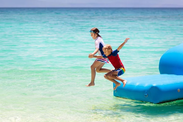 熱帯の海のビーチでトランポリンでジャンプする子供たち 子供たちは膨脹可能なウォータースライドでジャンプします エキゾチックな島のリゾートでアクアアミューズメントパーク 家族での休暇と子供との旅行 海沿岸の楽しみ — ストック写真