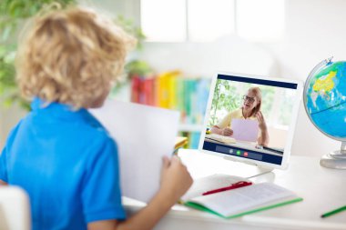 Çevrimiçi uzaktan öğrenme. Bilgisayarlı okul çocukları öğretmen ve sınıf grubuyla görüntülü konuşma yapıyorlar. Çocuk evden ders çalışıyor. Karantina ve koronavirüs salgını sırasında evde eğitim.