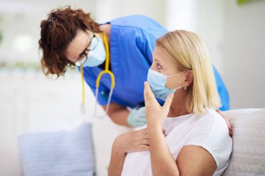 Doktor maske takan hasta hastayı muayene ediyor. Test ve tarama için sağlık kliniğindeki hasta kadın. Evde virüs tedavisi. Koronavirüs salgını. Covid-19 salgını. Kadın öksürüyor, göğsü ağrıyor..