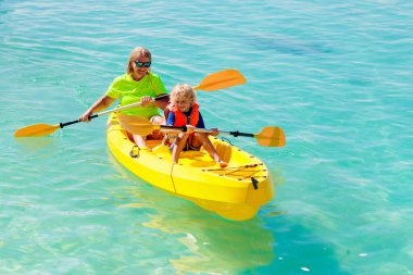Çocuklar okyanusta kayak yapıyor. Tropikal denizde kanodaki çocuklar. Genç bir çocukla aktif tatil. Ebeveynler, küçük bir oğlan ve güzel bir sahilde kanodaki bir kız. Çocukla birlikte tatil aktivitesi. Aile suyu eğlencesi.