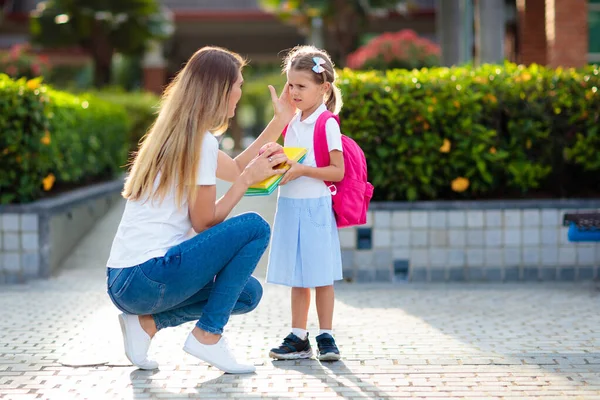 Mother and kids after school. Young mom picking up children after lessons in kindergarten or preschool. Pick up students. Boy and girl running to parents in school yard.