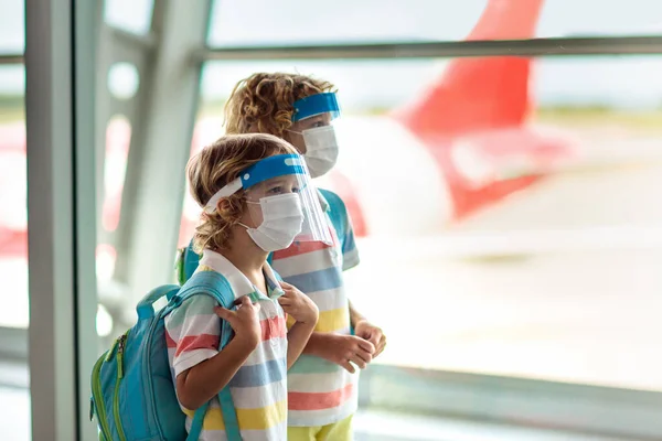 Family in airport in face shield and mask. Virus outbreak. Coronavirus and flu pandemic. Safe travel with young child and baby. Kids boarding airplane in surgical masks. Covid-19 pandemic.