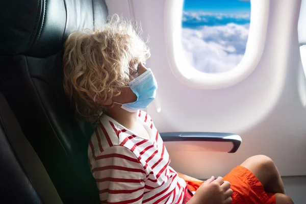 Child in airplane in face shield and mask. Flying with kids during virus outbreak. Vacation in coronavirus and flu pandemic. Safe travel with young child and baby. Kids fly airplane in surgical masks.