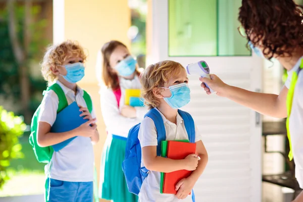 Temperature screening and medical check at school. Child in face mask in class in covid-19 outbreak. Teacher with thermometer at preschool entrance. Social distancing. Coronavirus prevention.