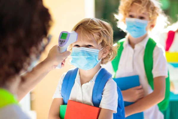 Temperature screening and medical check at school. Child in face mask in class in covid-19 outbreak. Teacher with thermometer at preschool entrance. Social distancing. Coronavirus prevention.