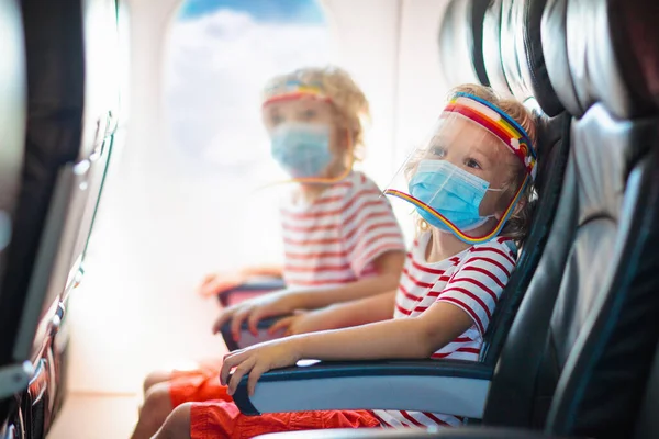 Child in airplane in face shield and mask. Flying with kids during virus outbreak. Vacation in coronavirus and flu pandemic. Safe travel with young child and baby. Kids fly airplane in surgical masks.