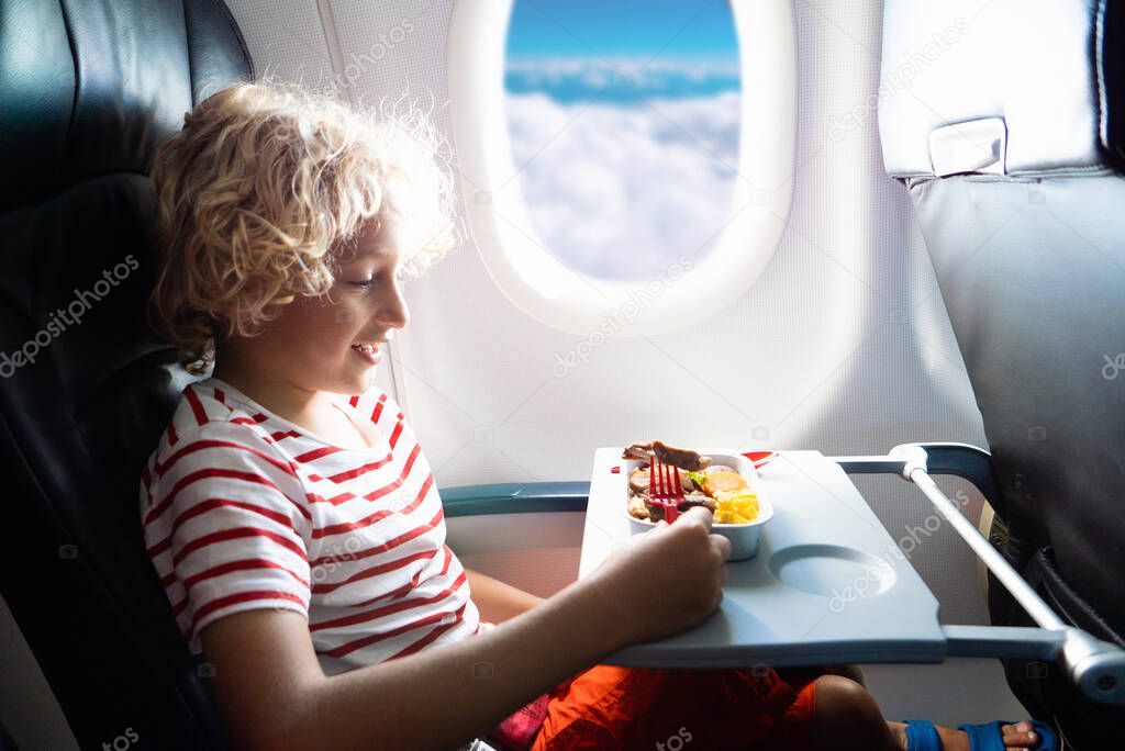 Child in airplane window seat. Kids flight meal. Children fly. Special inflight menu, food and drink for baby and kid. Boy eating healthy lunch in airplane. Travel and family vacation.  